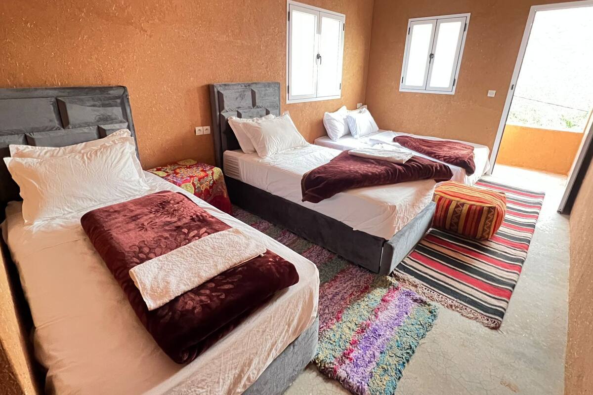 Habitación de hotel con tres camas, un colorido tapiz a rayas y vistas al exterior a través de las ventanas.