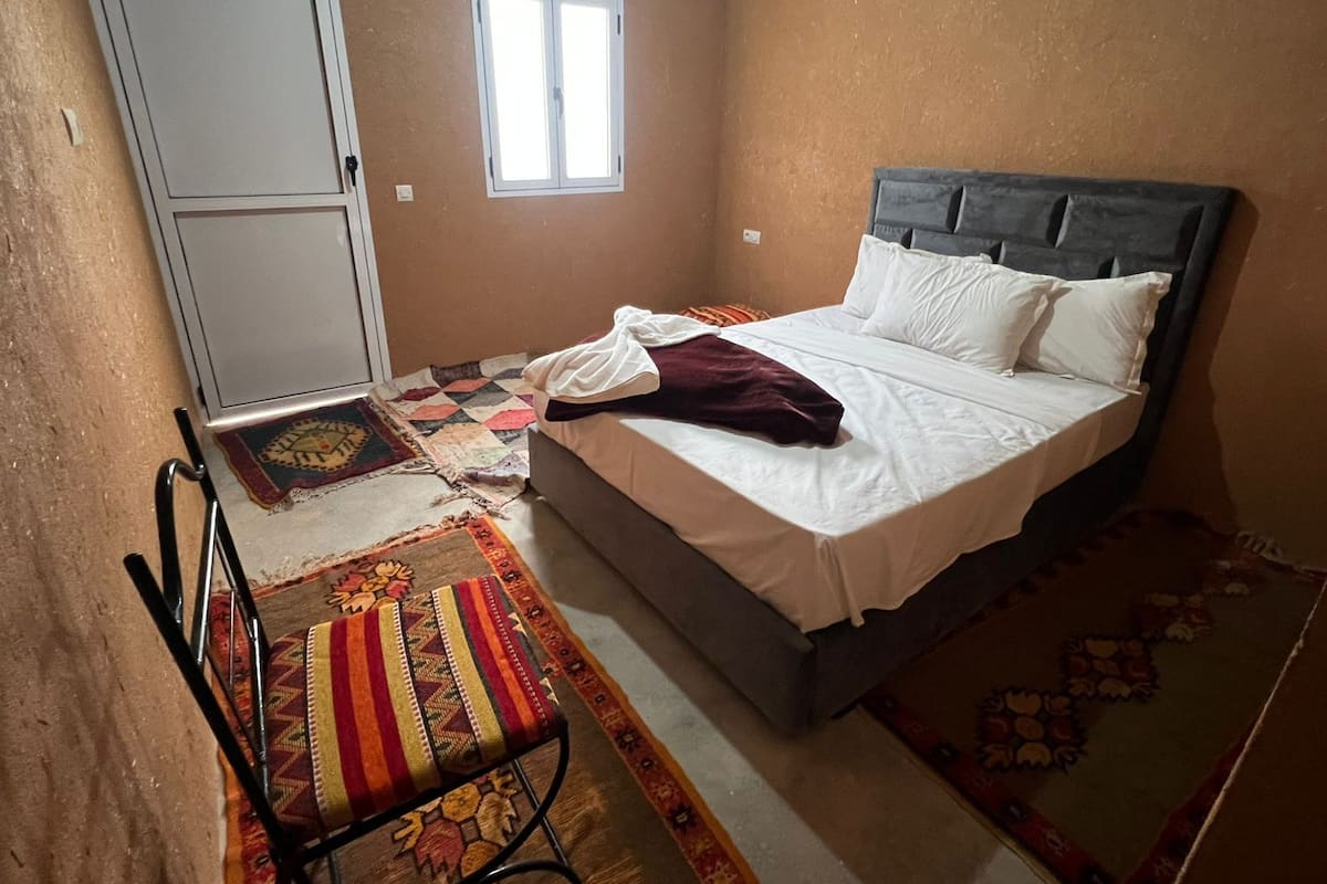 Un dormitorio con cama, ventana, puerta y sillón.