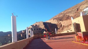 Una terraza en la azotea con vistas a un paisaje montañoso, una barandilla y una mesa con mantel de colores.