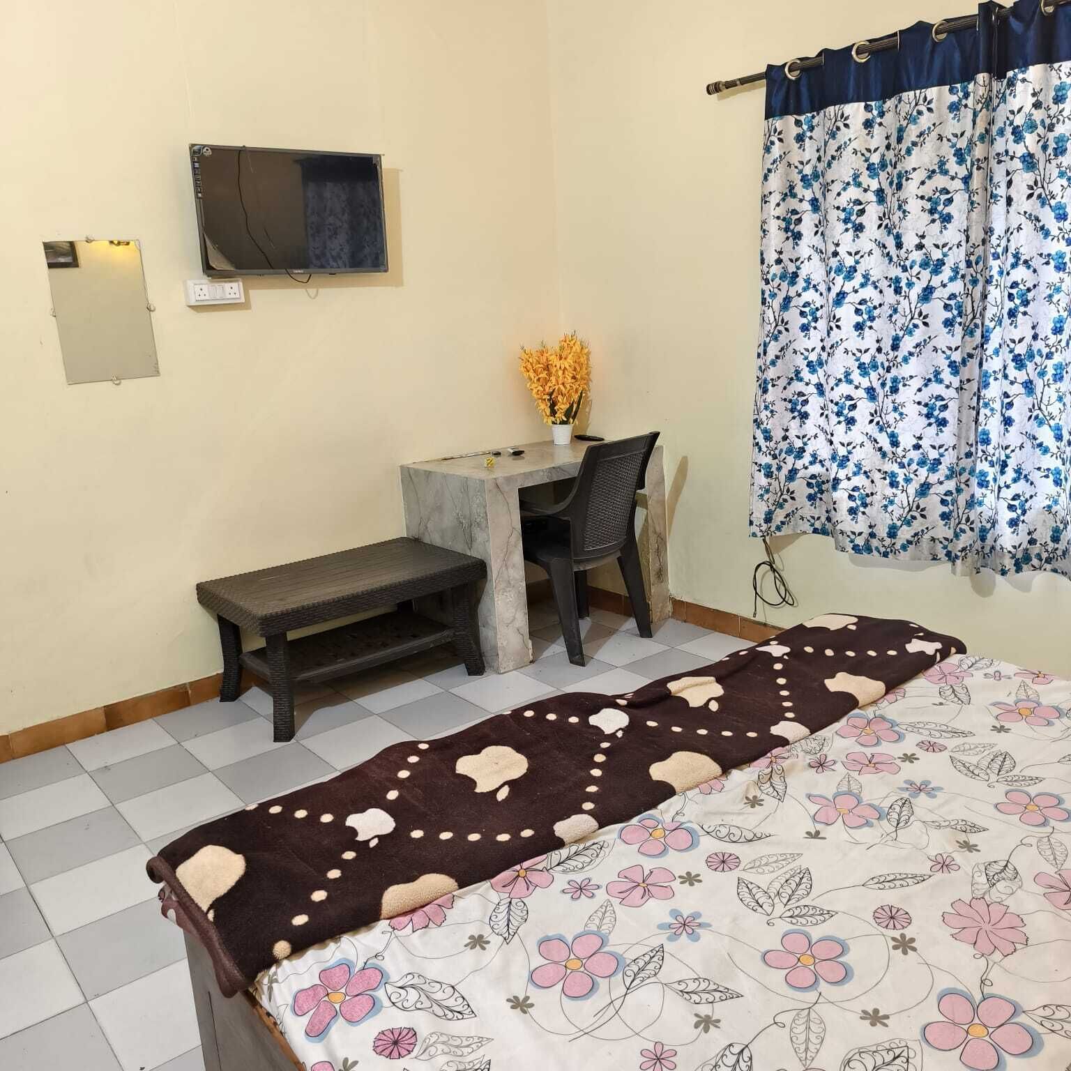 A room with a bed, a desk, a chair, a television on the wall, and a window with curtains.