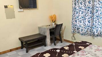 A room with a bed, a desk, a chair, a television on the wall, and a window with curtains.