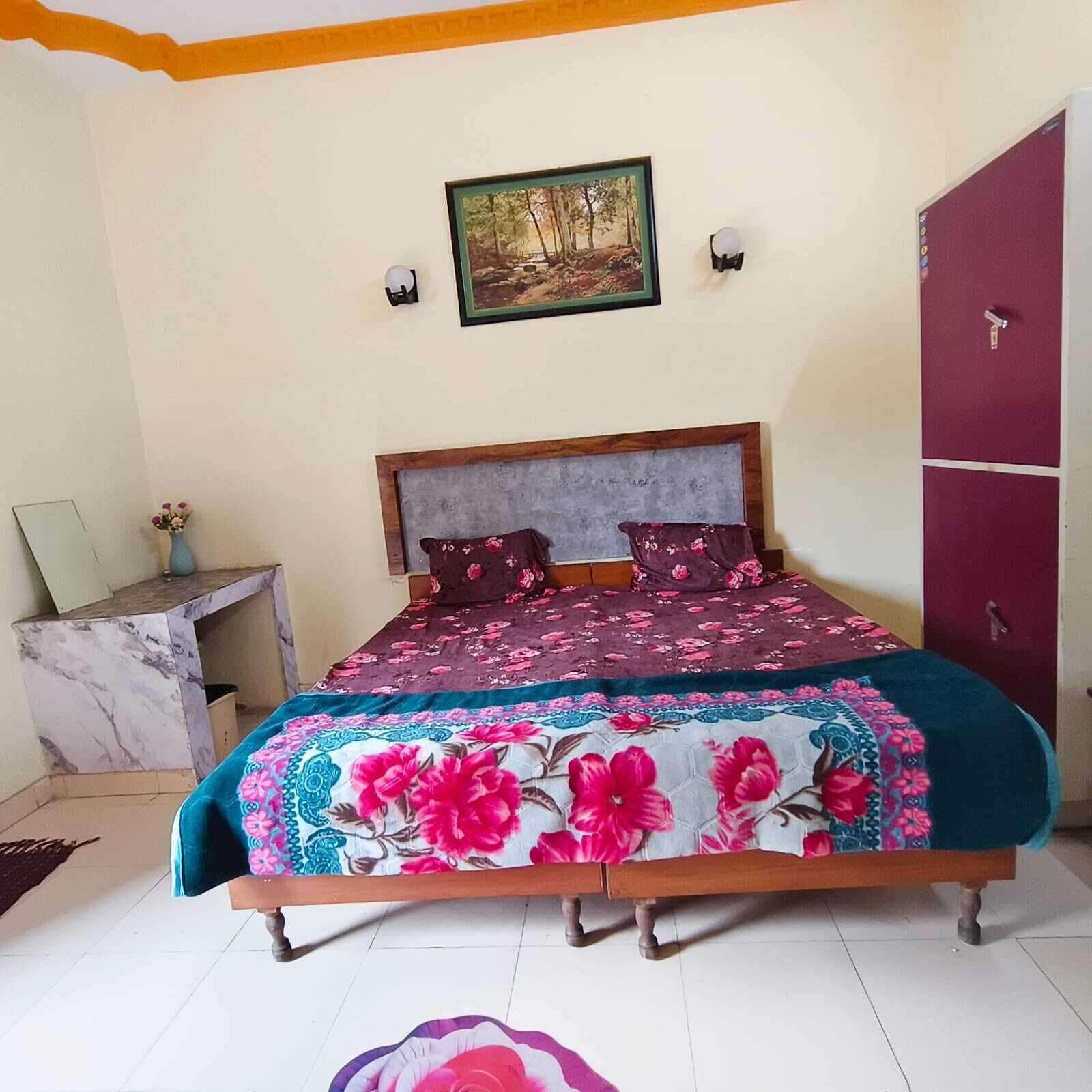 A bed with a floral bedspread, a nightstand with a vase, a painting on the wall, and a wardrobe.