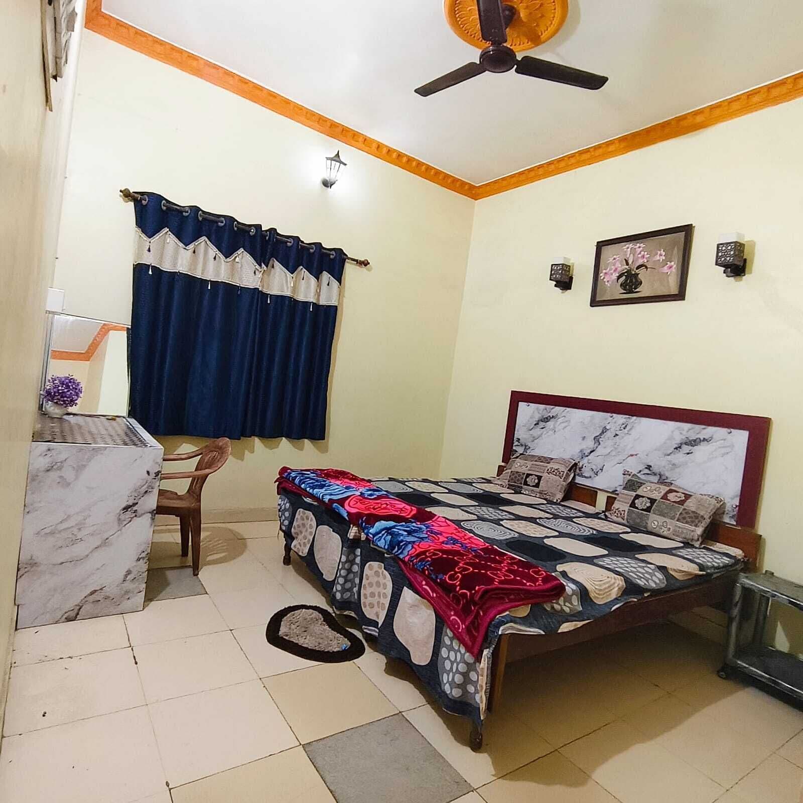 A bedroom with a bed, a desk, a chair, a ceiling fan, and a window with curtains.