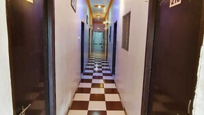 A hotel hallway with checkered flooring, numbered doors, and a ceiling with recessed lighting. - Hotel B B Pride (Raipur)