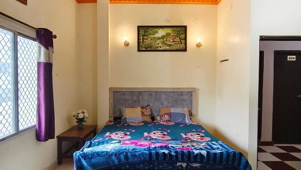 A bedroom with a bed, a ceiling fan, a window with curtains, a door, and a wall-mounted picture. - Hotel B B Pride (Raipur)