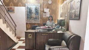 A reception desk with a sign, a staircase, a checkered floor, and a wall with framed pictures. - Hotel B B Pride (Raipur)