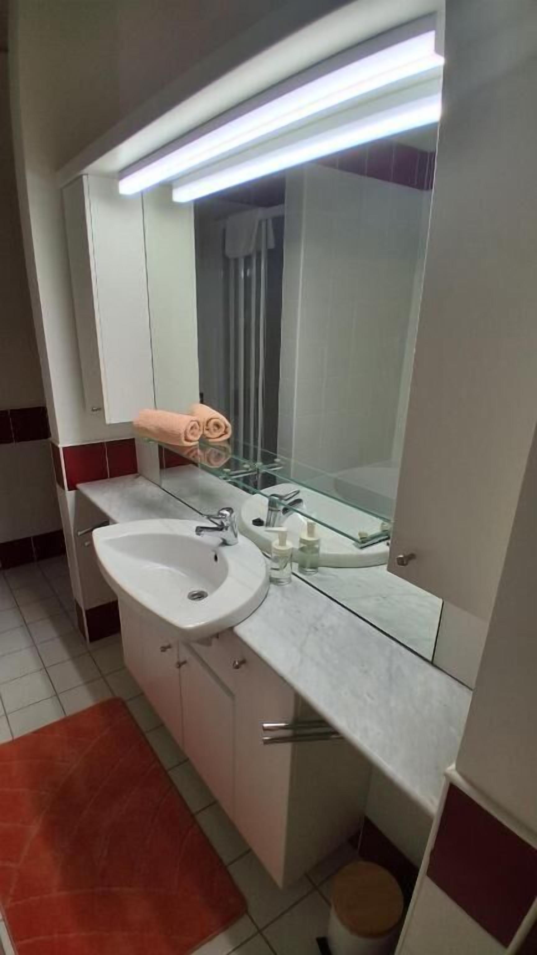 A bathroom with a white sink, a mirror, and a glass shelf.