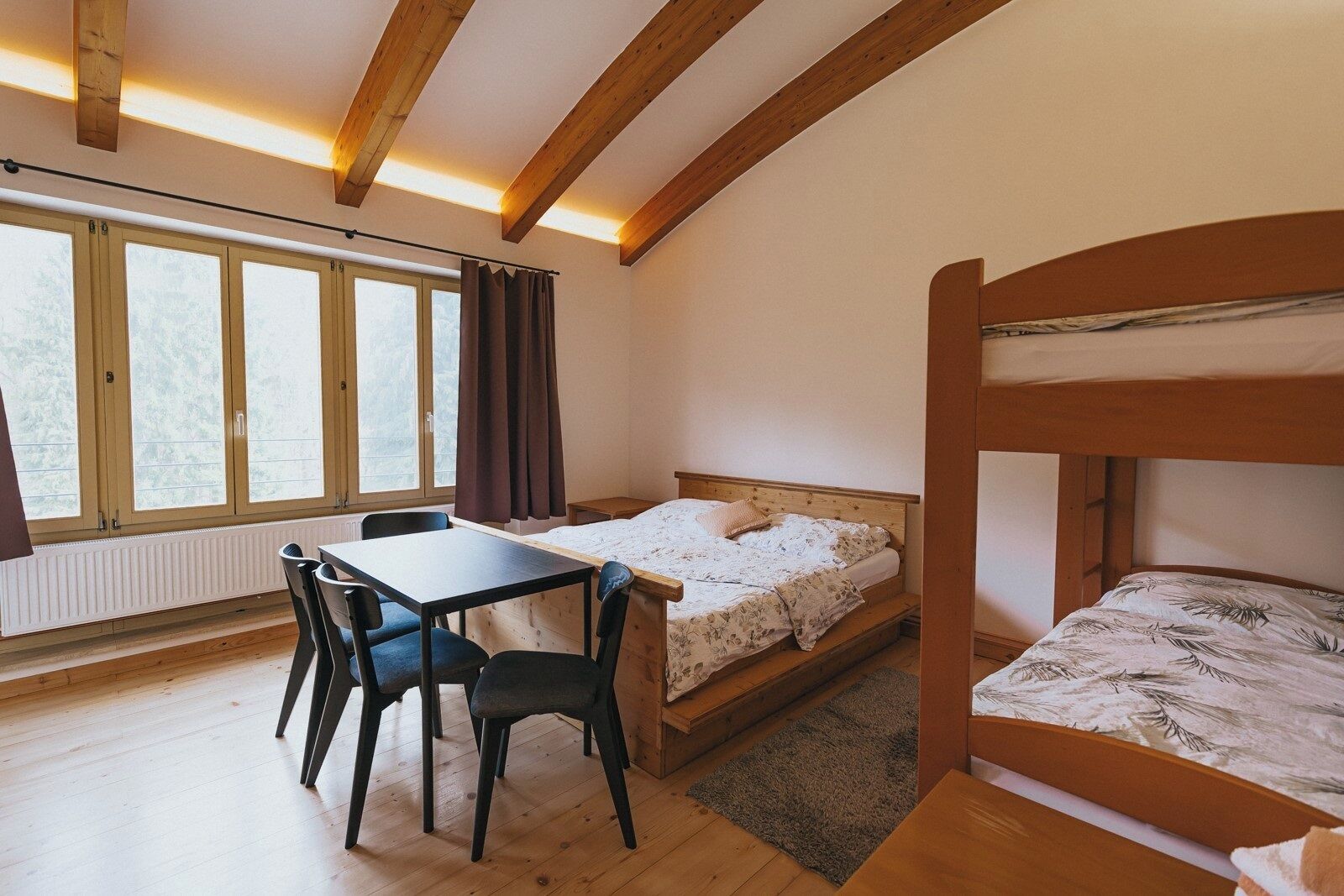 A room with a bunk bed, a desk with chairs, a window with curtains, and a radiator.