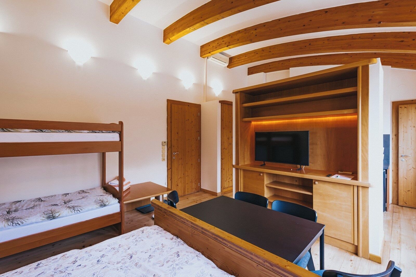 Una habitación con literas, un escritorio, una silla, un televisor y estanterías empotradas.