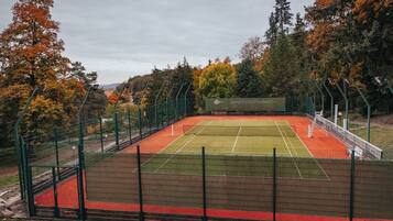A tennis court with a net, surrounded by a green fence, and trees in the background.