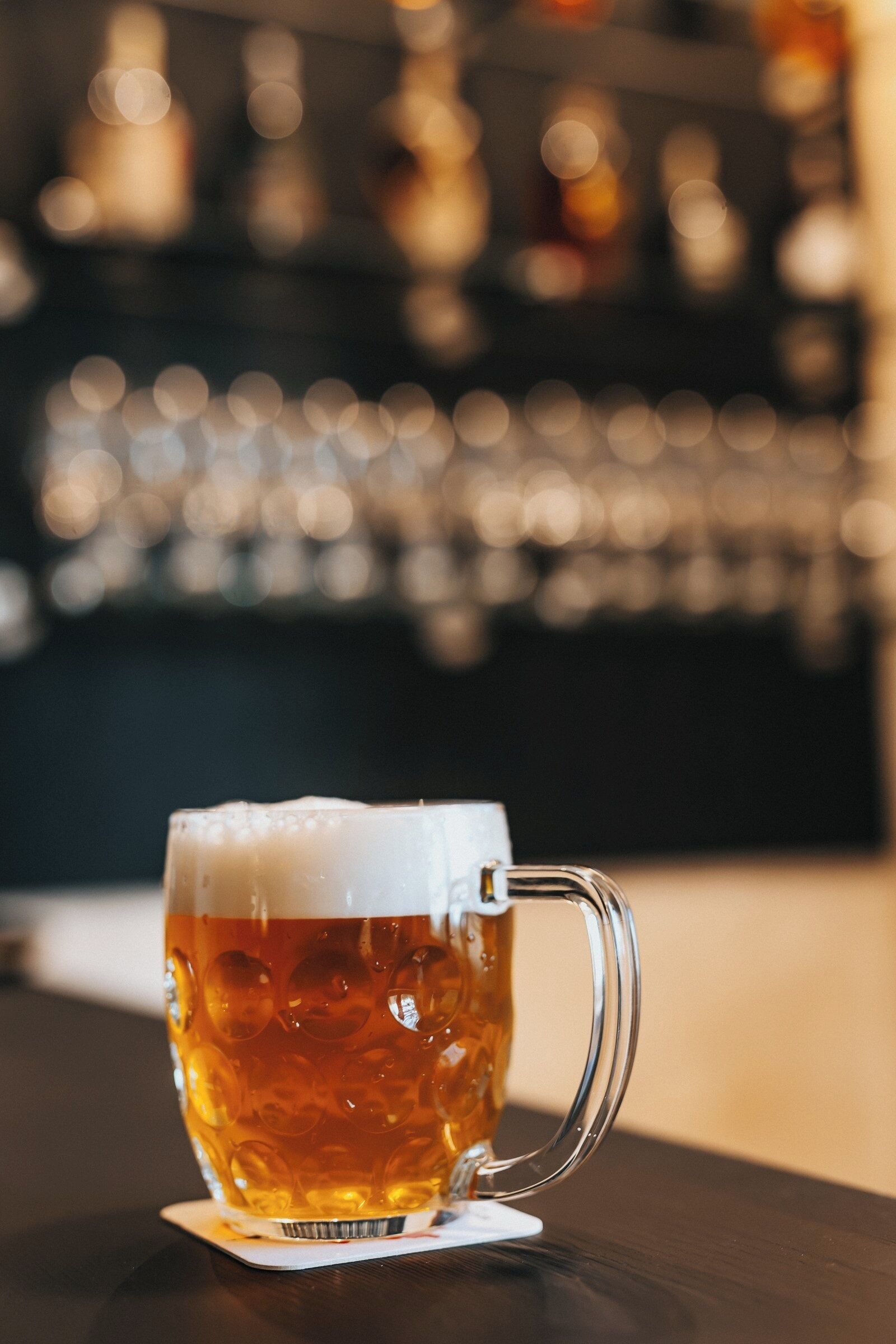 A glass mug with a handle, filled with a golden liquid, on a coaster.