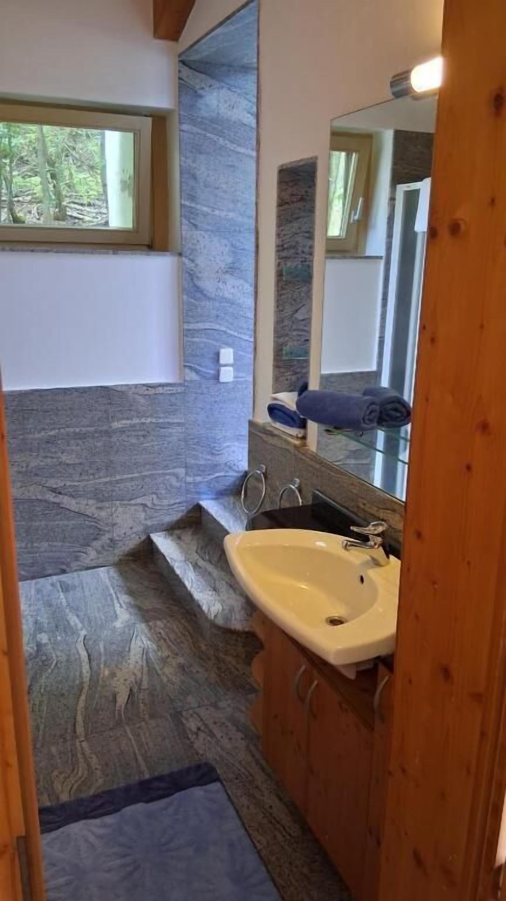 Une salle de bain avec un sol en pierre, un lavabo et un miroir.
