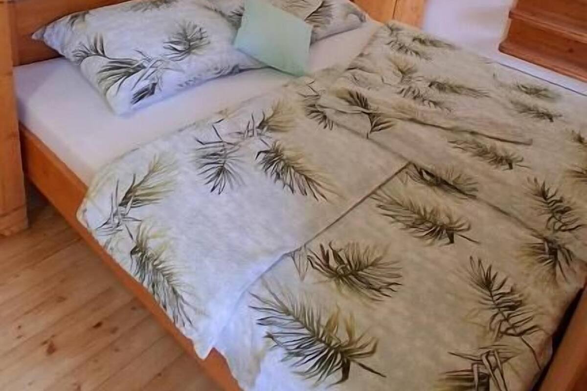 A single bed with a floral bedspread, a wooden wardrobe, and a wall-mounted light fixture.