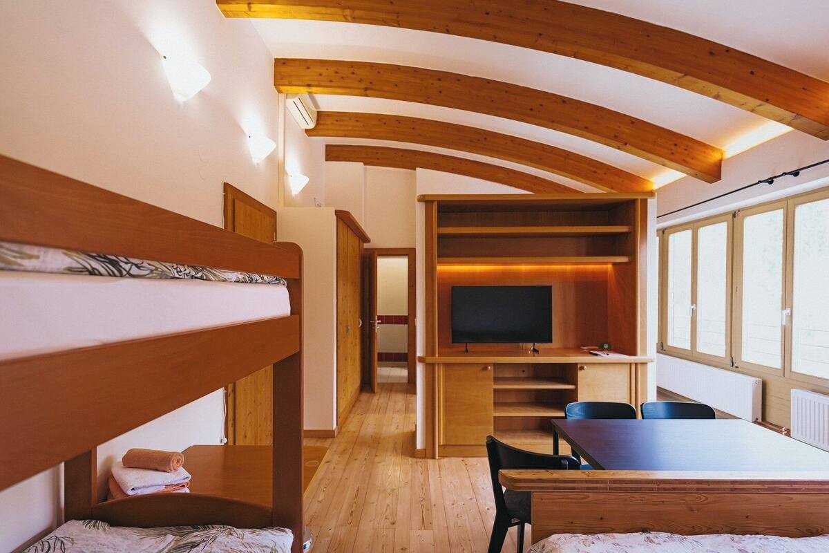 A room with bunk beds, a TV, a dining table, and a window with a view.