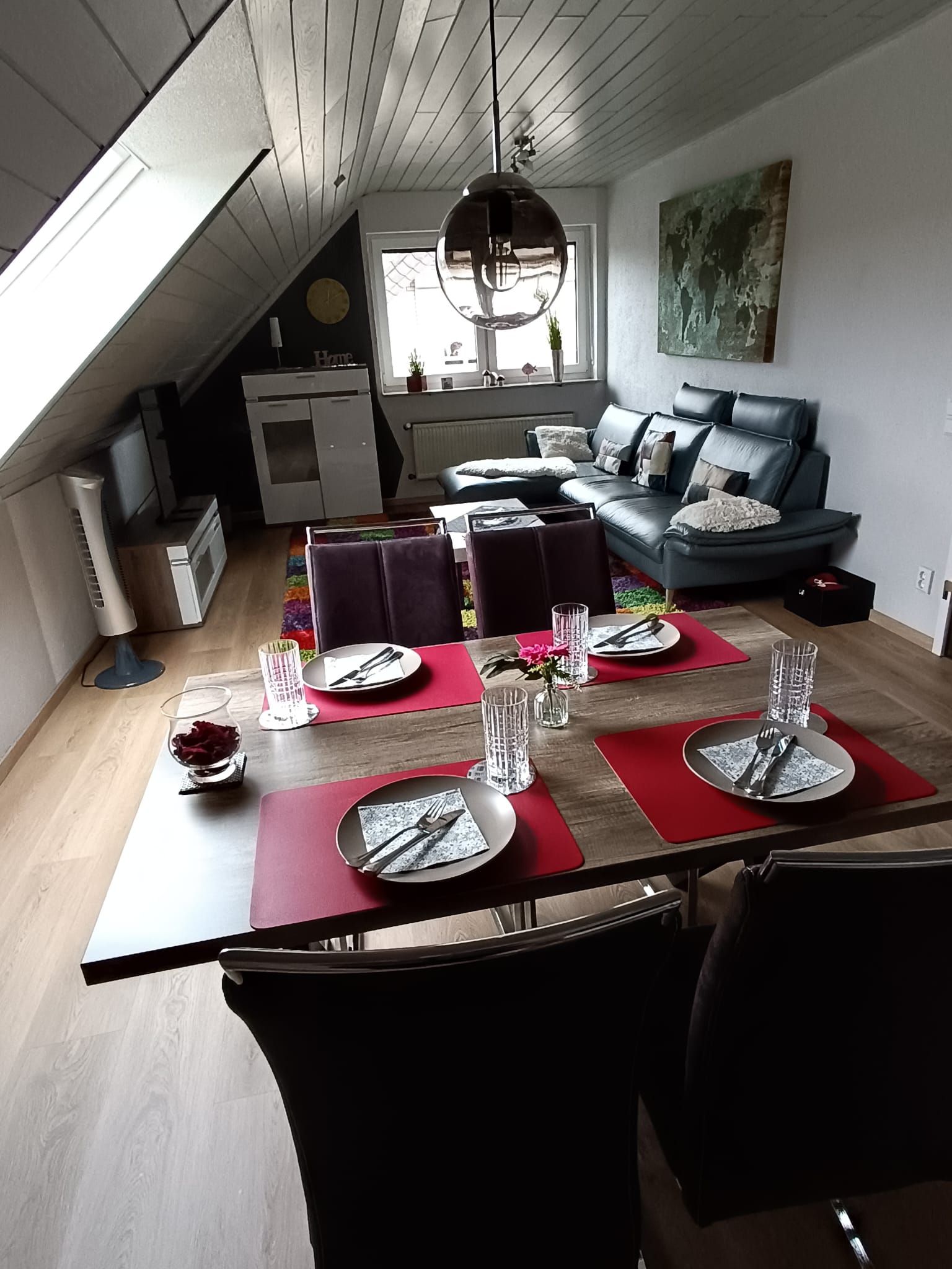 Et spiseområde med et bord dækket til fire personer, en sofa og et køkken i baggrunden.