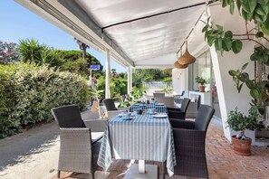 Eine Terrasse im Freien mit Korbmöbeln, einem Tisch mit gestreiftem Tischläufer und Topfpflanzen.