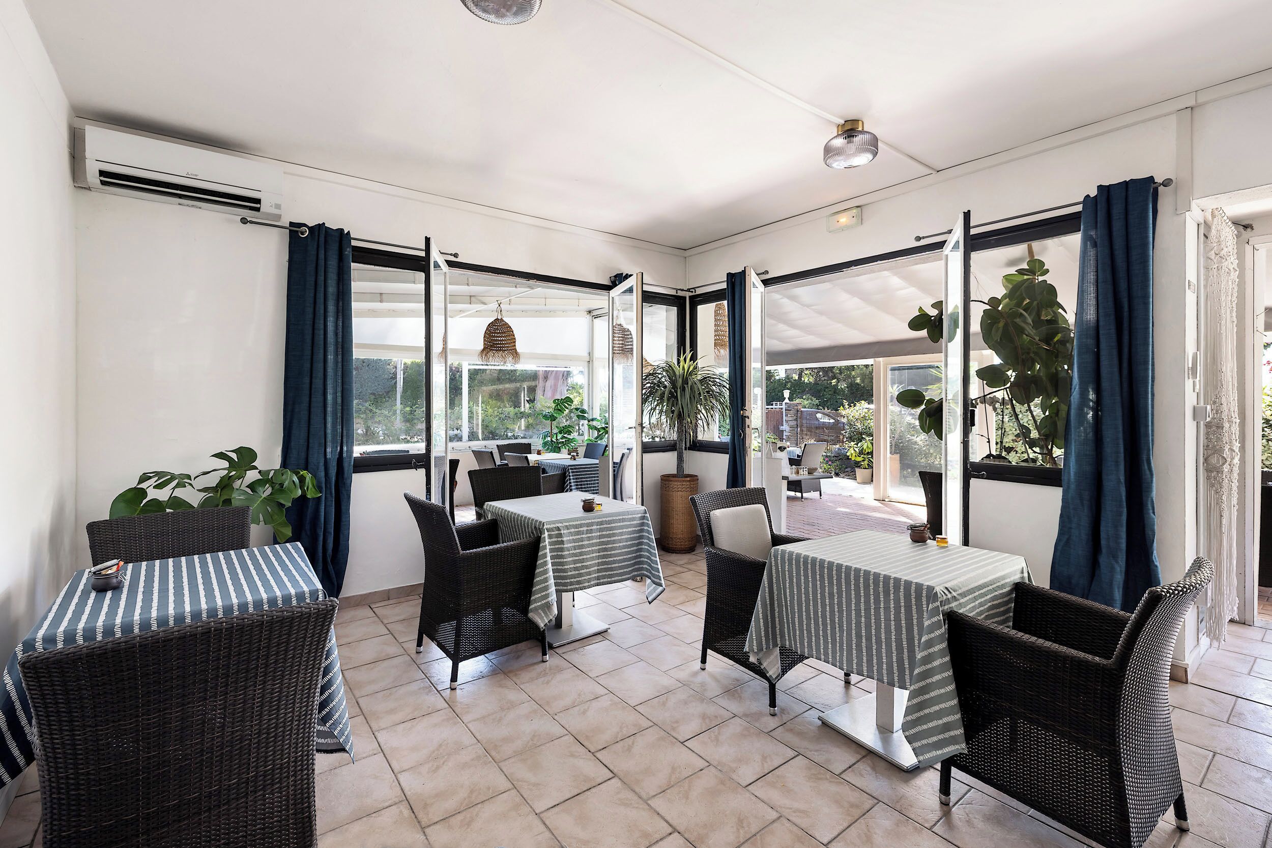 A sunlit patio area with wicker furniture, large windows, and potted plants.