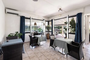 A sunlit patio area with wicker furniture, large windows, and potted plants. - Hôtel Le golfe bleu (Cavalaire-sur-Mer)
