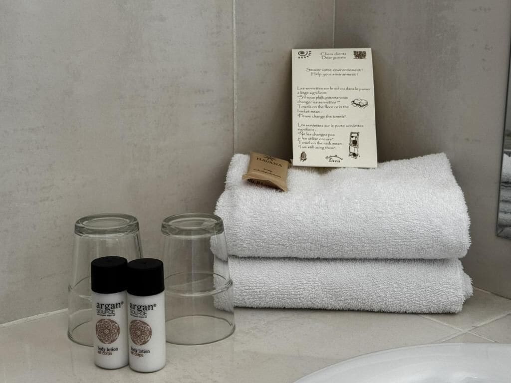 A bathroom with a white towel, two bottles of argan oil, and a sign with instructions.