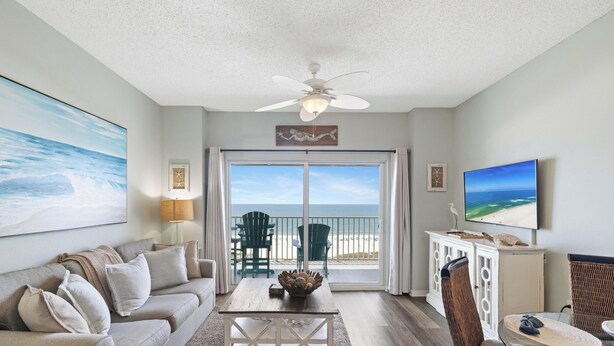 Un salon avec vue sur la plage, un ventilateur de plafond, un téléviseur et un coin repas.