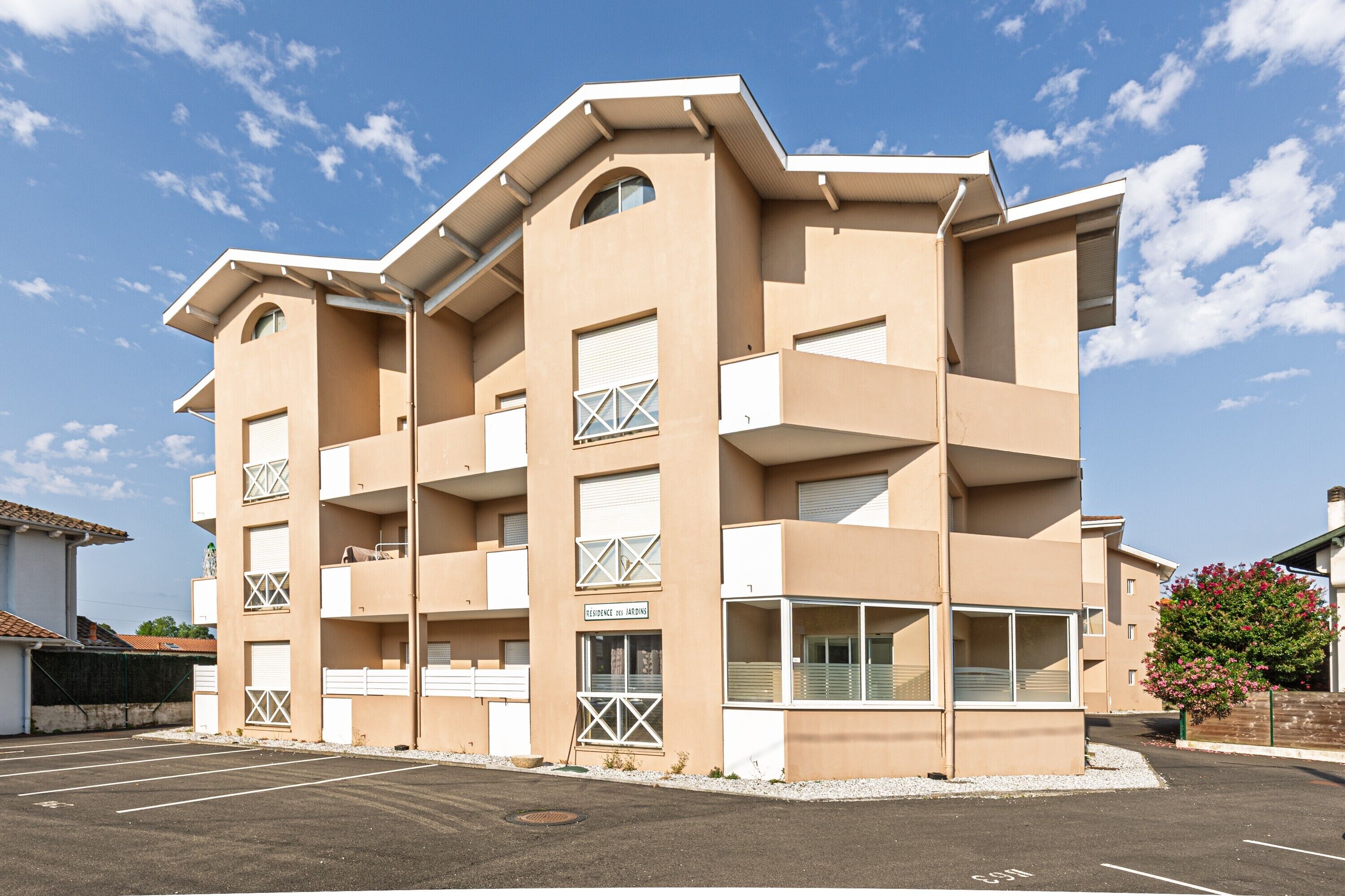 Un edificio de varios pisos con balcones, un estacionamiento y un cielo despejado.