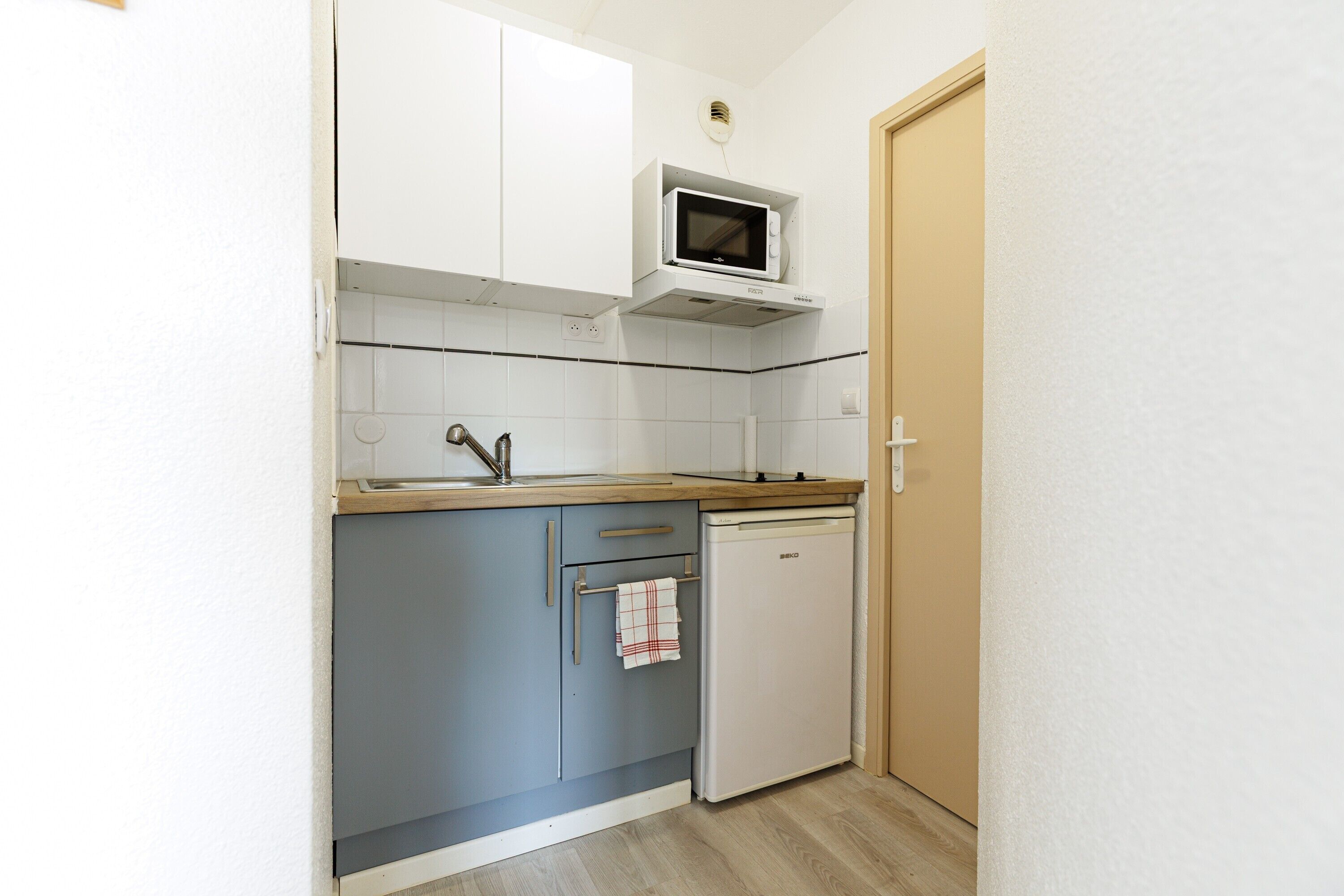 Een kleine keuken met witte kastjes, een magnetron, een spoelbak en een vaatwasser.