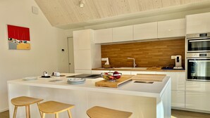 Una cucina moderna con isola centrale, sgabelli in legno, una macchina per caffè e una schiena di legno.
