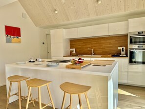 Eine moderne Küche mit einer zentralen Kochinsel, Holzstühlen, einer Kaffeemaschine und einer Holzrückwand.