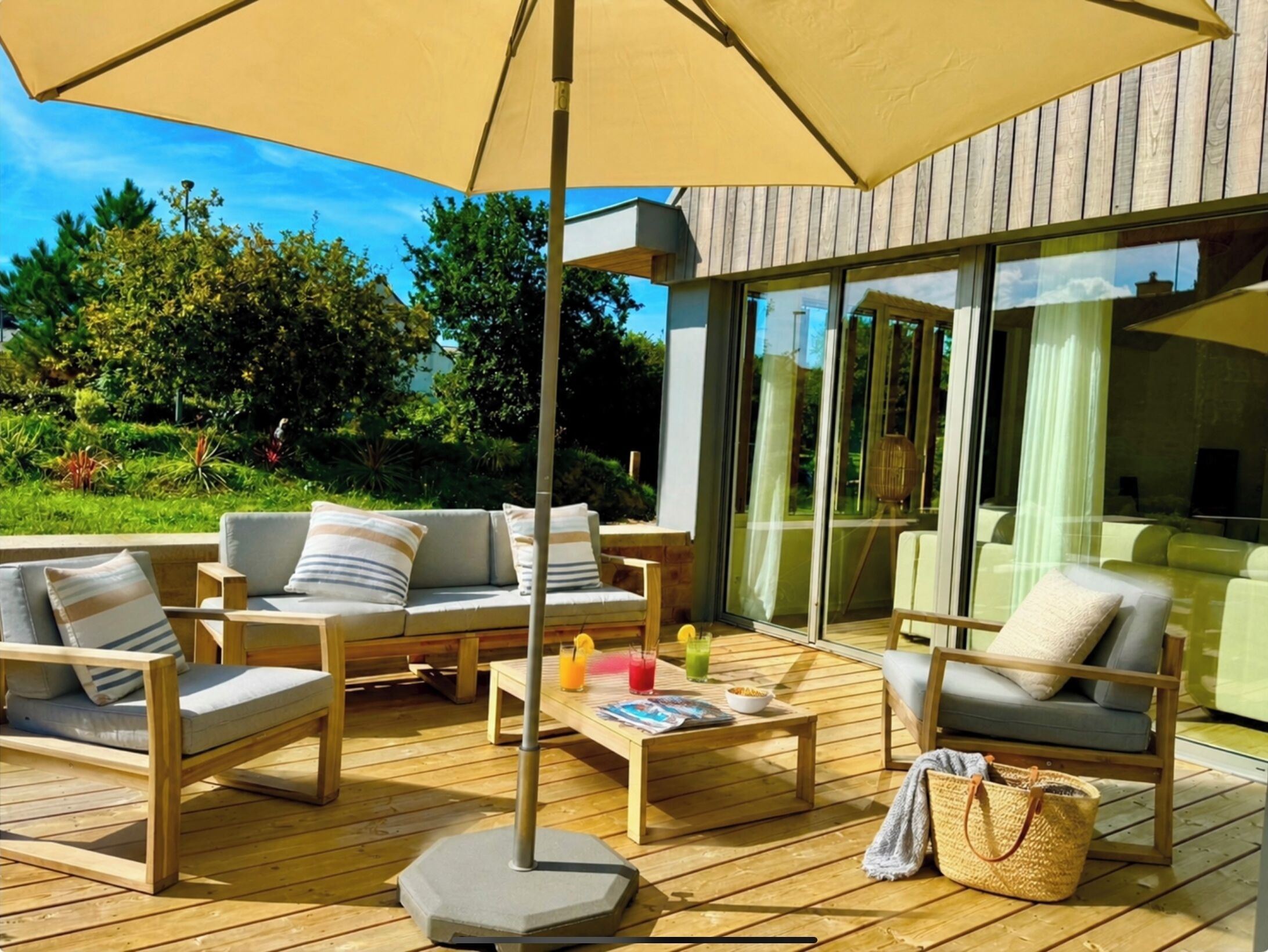 An outdoor deck with wooden furniture, a table with drinks, and a large umbrella.