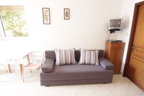Ein Wohnzimmer mit einer Couch, einem Sessel, einem Fernseher und einem Schrank.