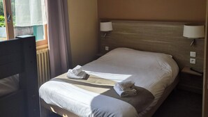 Una habitación de hotel con una cama, dos lámparas de noche, una silla y un ventanal con cortinas.