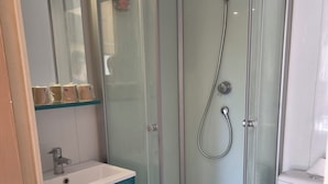 Un baño con ducha envuelta en vidrio, inodoro blanco, lavamanos con grifo y espejo sobre el lavamanos.