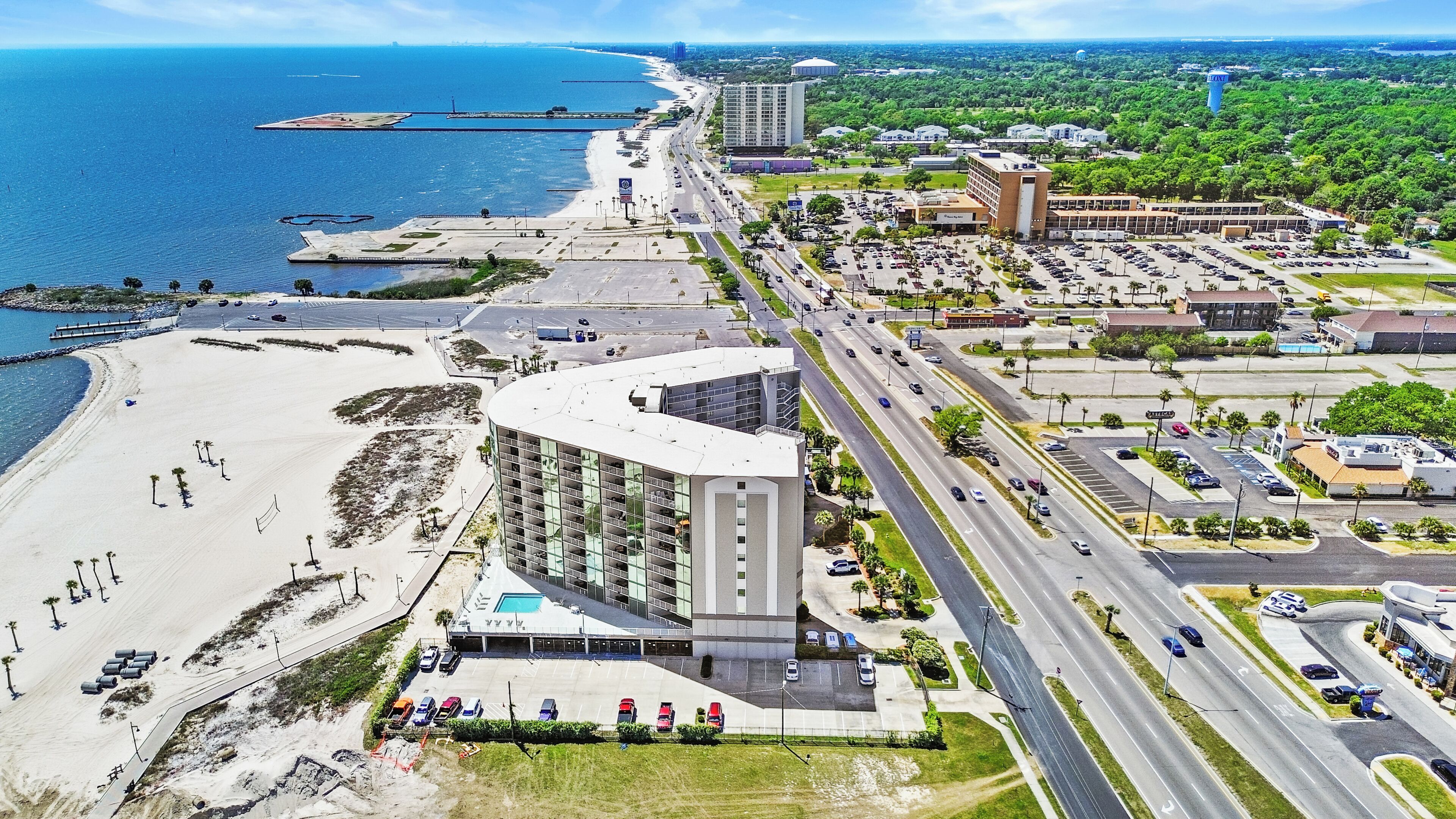 A coastal hotel with a pool, adjacent beach, and a parking lot.
