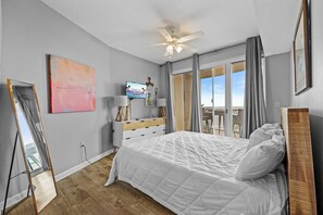 Ein Schlafzimmer mit einem Bett, einem Fernseher, einer Kommode, einem Deckenventilator und einem großen Fenster.