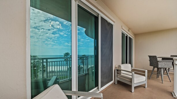 Een balkon met uitzicht op de oceaan, een zithoek met rieten meubels en een witte bank.