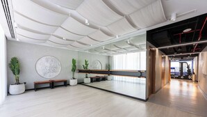 A spacious room with a large mirror, wooden benches, potted plants, and a modern ceiling design. - StayShort - Elegant 1BR in Prime Business Bay (Business Bay)
