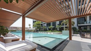 A modern outdoor pool area with lounge chairs and a wooden pergola. - StayShort - Elegant 1BR in Prime Business Bay (Business Bay)