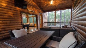Eine Blockhütte mit Holzinnenausstattung, einem Essbereich mit Tisch und Stühlen sowie Blick auf den Wald durch große Fenster.