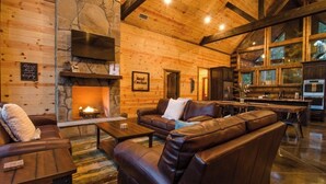 Ein gemütliches Blockhaus-Interieur mit Kamin aus Stein, Ledersofas, einem Essbereich und einer Küche.