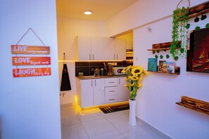 Eine moderne Küche mit weißen Schränken, einer Mikrowelle und einem Spülbecken. Eine Wandtafel zeigt inspirierende Worte und ein Blumentopf mit gelben Blüten.