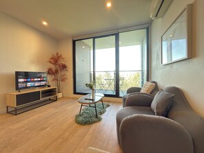 Ein modernes Wohnzimmer mit Fernseher, einer Couch, einem kleinen Tisch und einer Zimmerpflanze.