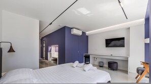A modern hotel room with a large bed, a desk with a flat-screen TV, a walk-in closet, and a bathroom with a mirror and towel rack. - Violet Studio 113 Love in Colours Collection (Durrës)