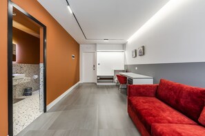 Een moderne hotelkamer met een rode bank, een klein bureau en een kitchenette.