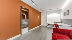Quarto de hotel moderno com parede de destaque laranja, uma cadeira vermelha, uma pia branca e um espelho grande.