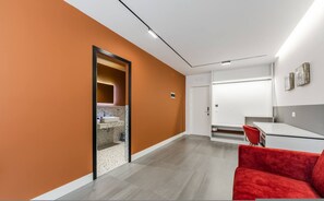 Ein modernes Hotelzimmer mit einer orangefarbenen Akzentwand, einem roten Sessel, einem weißen Waschbecken und einem großen Spiegel.