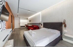 Een moderne hotelkamer met een groot bed, een rode bank, een flatscreen-tv en een klein eethoekje.