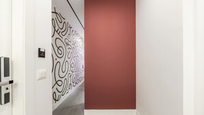 A hallway with a patterned wall, a red door, and a doorbell. - Rose Studio 112 Love in Colours Collection (Durrës)