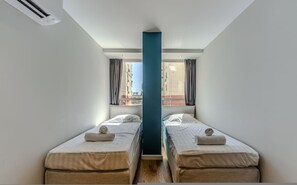 Ein Zimmer mit zwei Betten, einer zentralen Säule und Blick auf die äußere Bebauung.