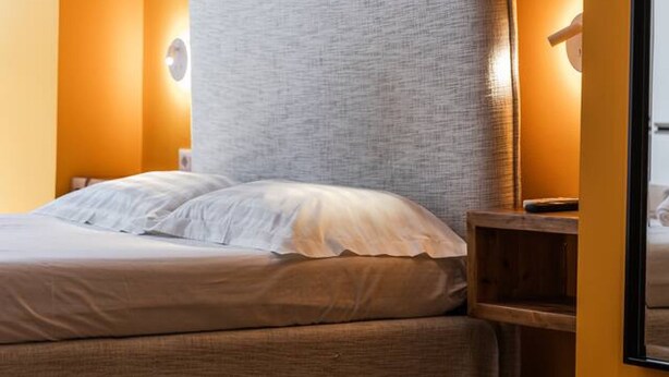 A bed with a grey headboard in a room with orange walls and wooden flooring. - Orange Studio 104 Love in Colours Collection (Durrës)