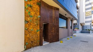 A building entrance with a textured wall, a door with a logo, and a clear sky. - Orange Studio 104 Love in Colours Collection (Durrës)